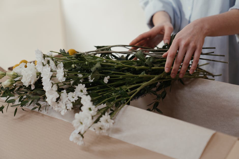 A floral delivery courier, wearing a red cap and high-visibility yellow vest over a white t-shirt, is delivering a bouquet of fresh white hydrangeas with green foliage. The bouquet is wrapped in clear