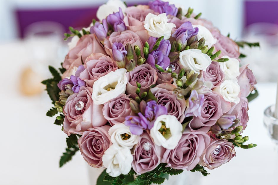 A bride holding a large, lush bouquet arrangement featuring a mixture of flowers in soft pink, purple, white, and deep maroon shades. The bouquet includes roses, lisianthus, and chrysanthemums, accent